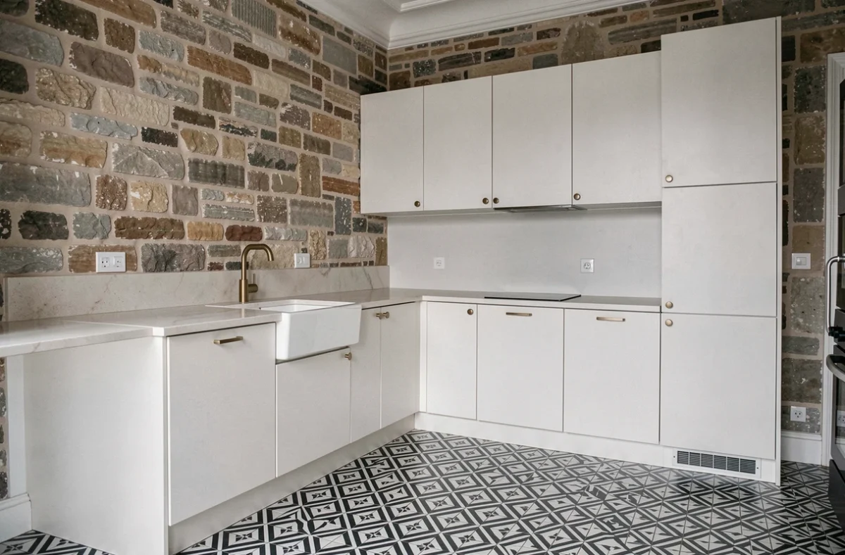 Cuisine rénovée d'un appartement haussmannien mêlant pierre apparente, carrelage géométrique et robinetterie en laiton brut